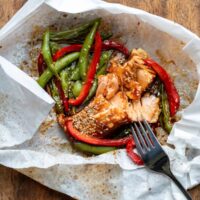Close up of a fork flaking salmon fillets in a microwave salmon parcel with vegetables and teriyaki sauce.