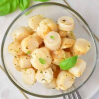 Looking down at a glass bowl of boiled scallops in garlic butter.