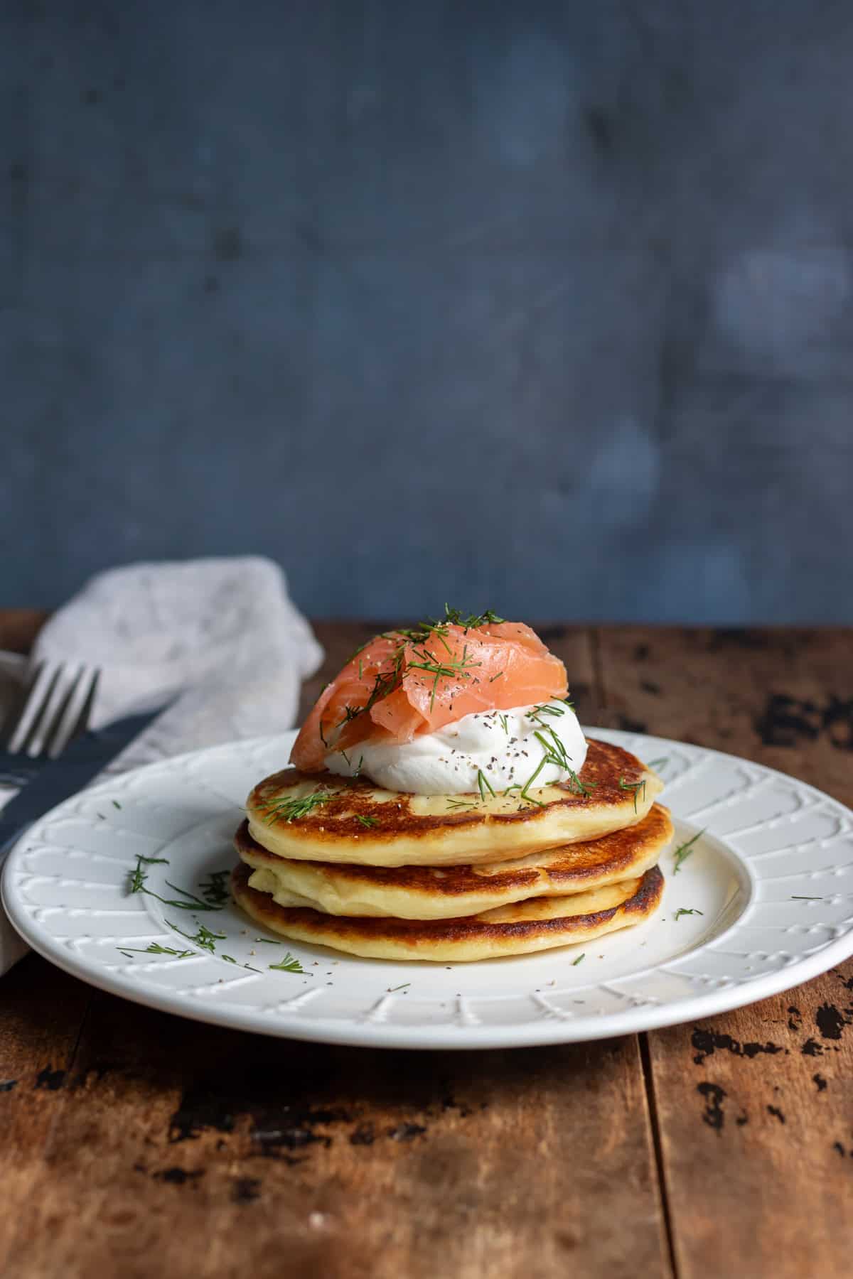 A stack of mashed potato pancakes on a plate, topped with sour cream and smoked salmon.