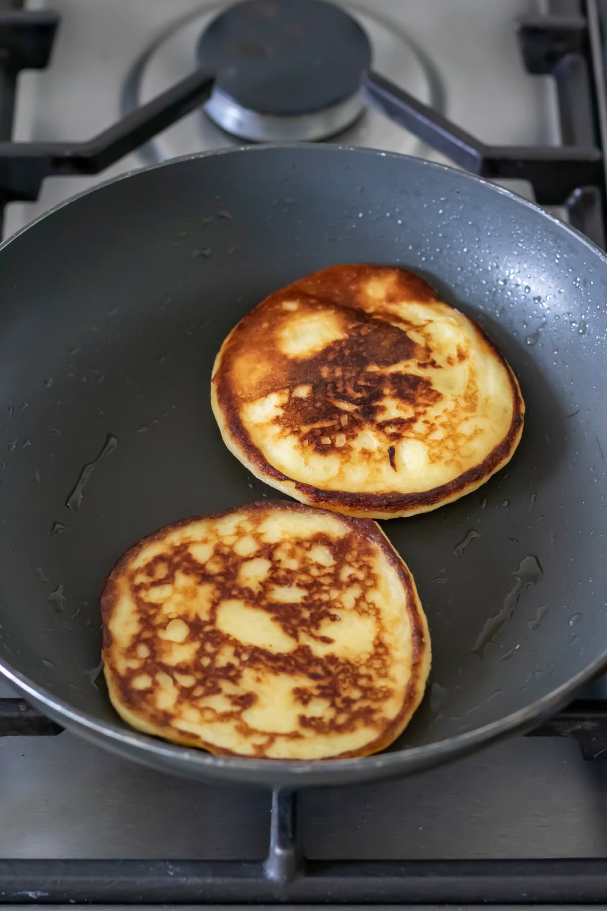 Two mashed potato pancakes are cooking in a pan on the stove.