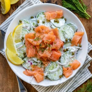 A bowl of smoked salmon cucumber salad on a table.