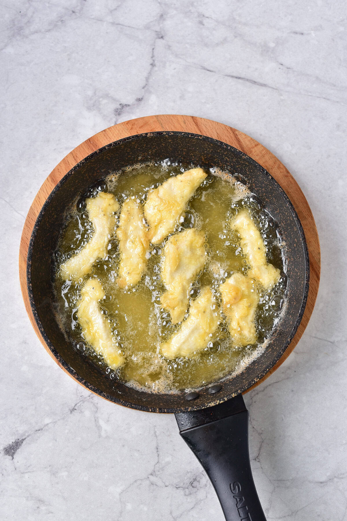 Frying the coated chicken strips.