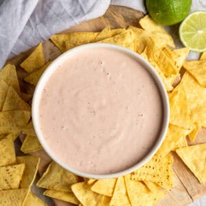 Looking down at a table scattered with tortilla chips around a dish of mexican ranch dip.