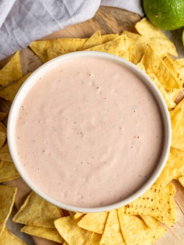 Looking down at a table scattered with tortilla chips around a dish of mexican ranch dip.