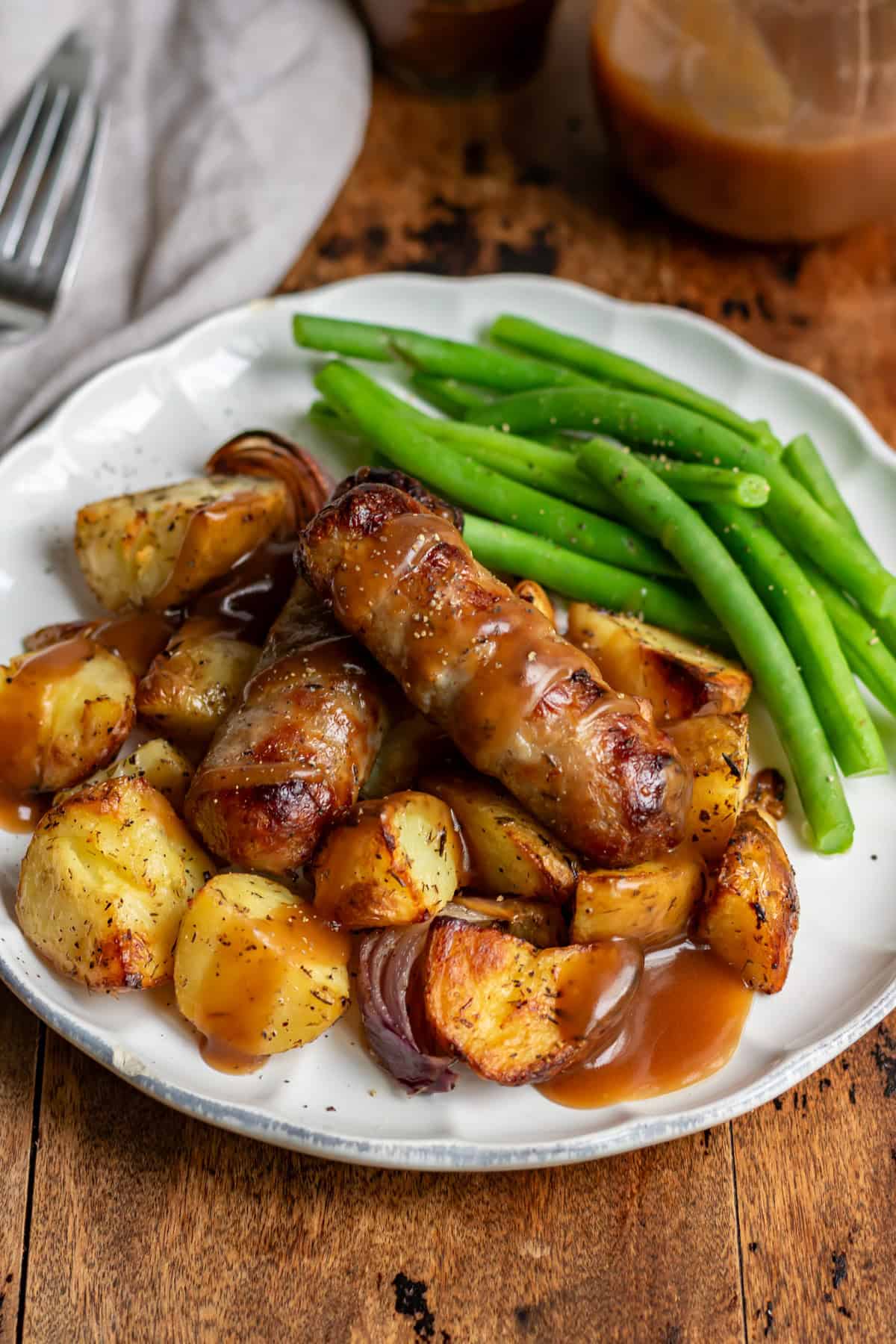 Close up of a wooden table with a plate of beans, potatoes and sausage bake.