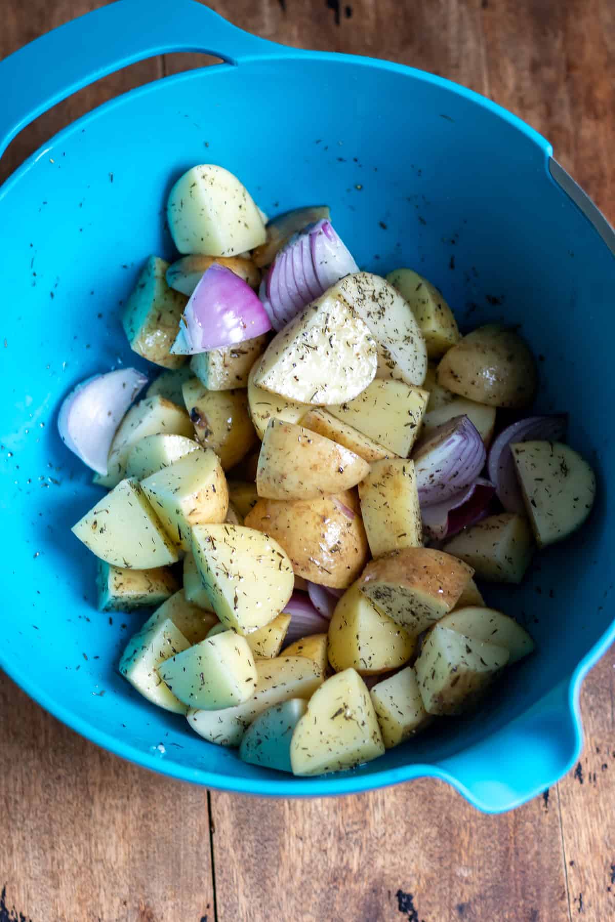 A mixing bowl with potatoes, onions and herbs.