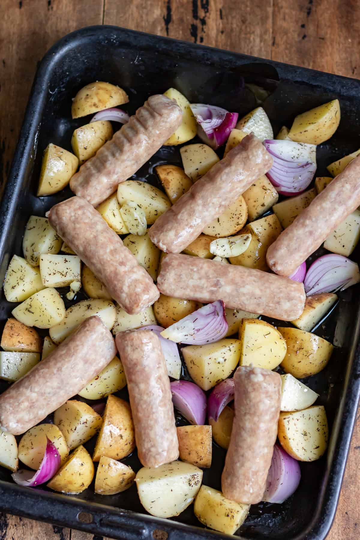 Potatoes and onions on the baking sheet, topped with sausages.