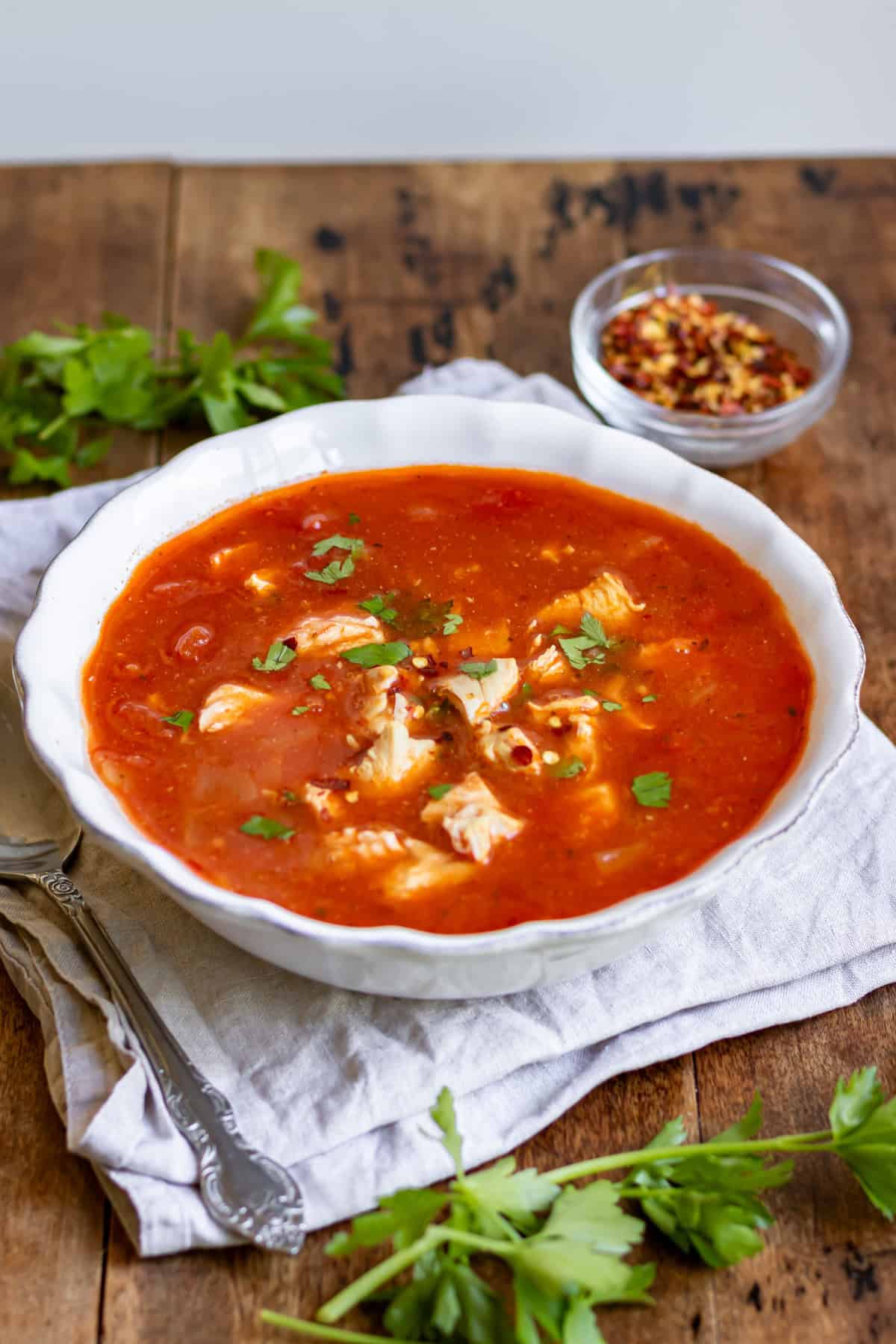 Wooden table with a bowl of spicy chicken soup.