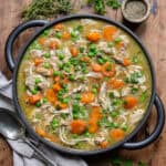 Wooden table with a dish of slow cooker chicken casserole, next to a napkin, pot of pepper and some herbs.