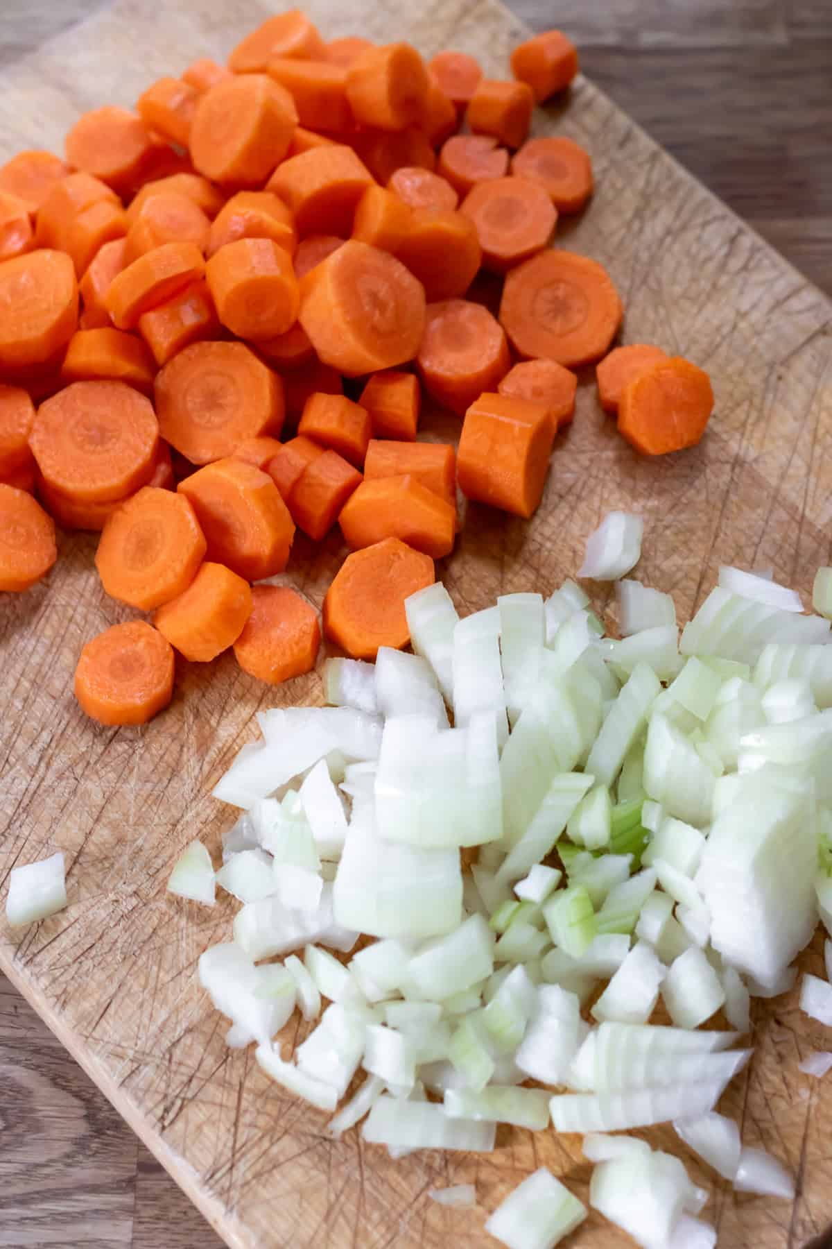 Chopped onion and carrots on a cutting board.