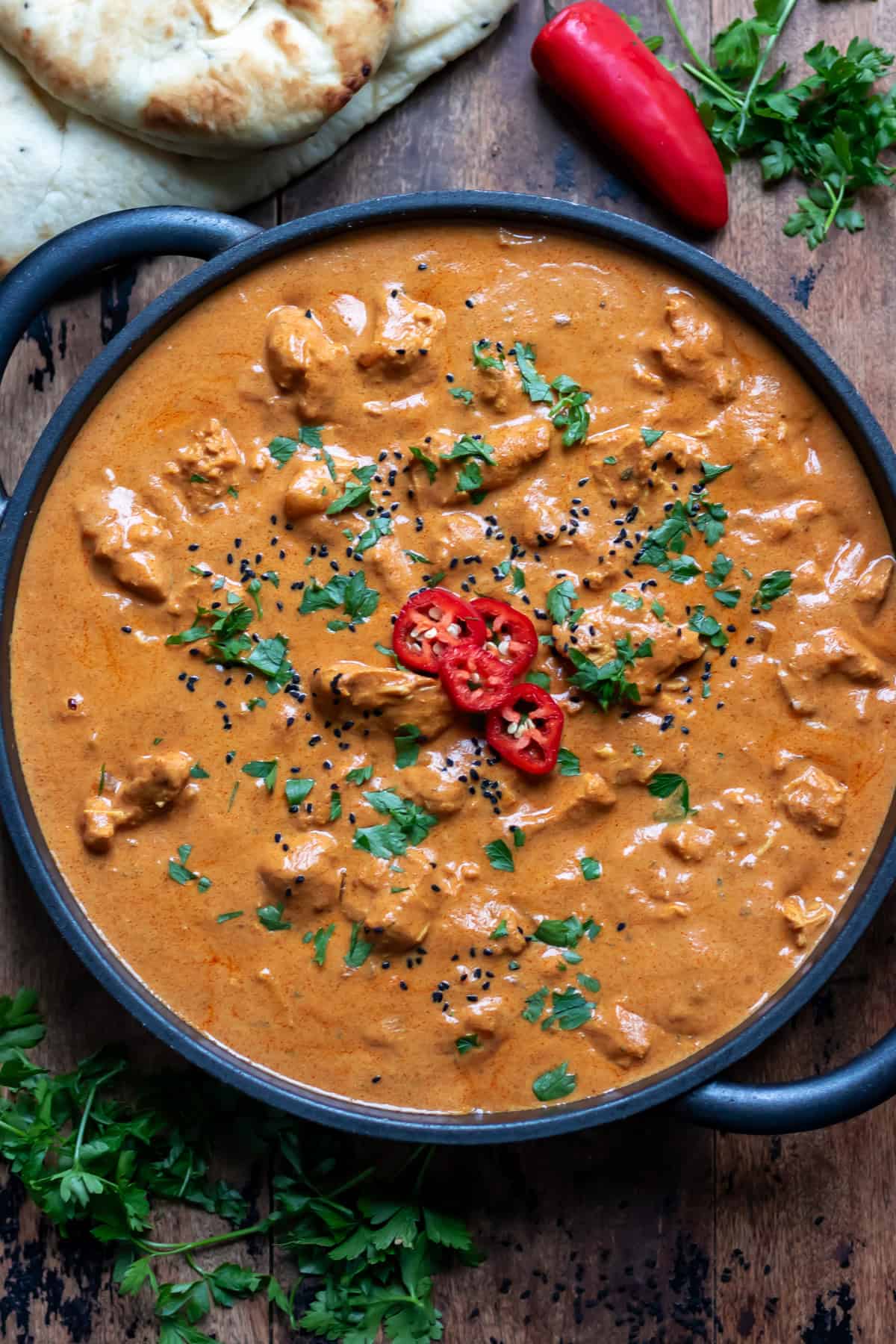 Serving dish of slow cooker chicken tikka masala topped with coriander, onion seeds and chopped red chili.