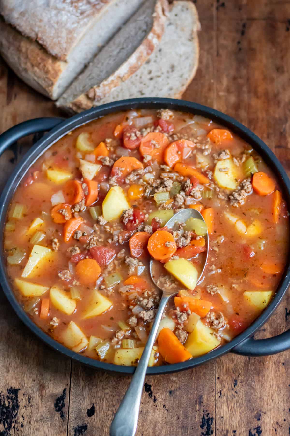 Serving dish of ground beef soup on a table next to a loaf of bread.