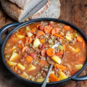 Close up of a spoon in a serving dish of ground beef soup with potatoes.
