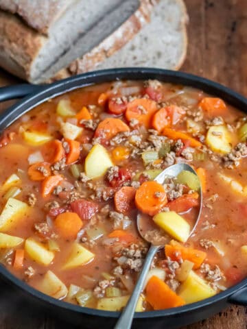 Close up of a spoon in a serving dish of ground beef soup with potatoes.