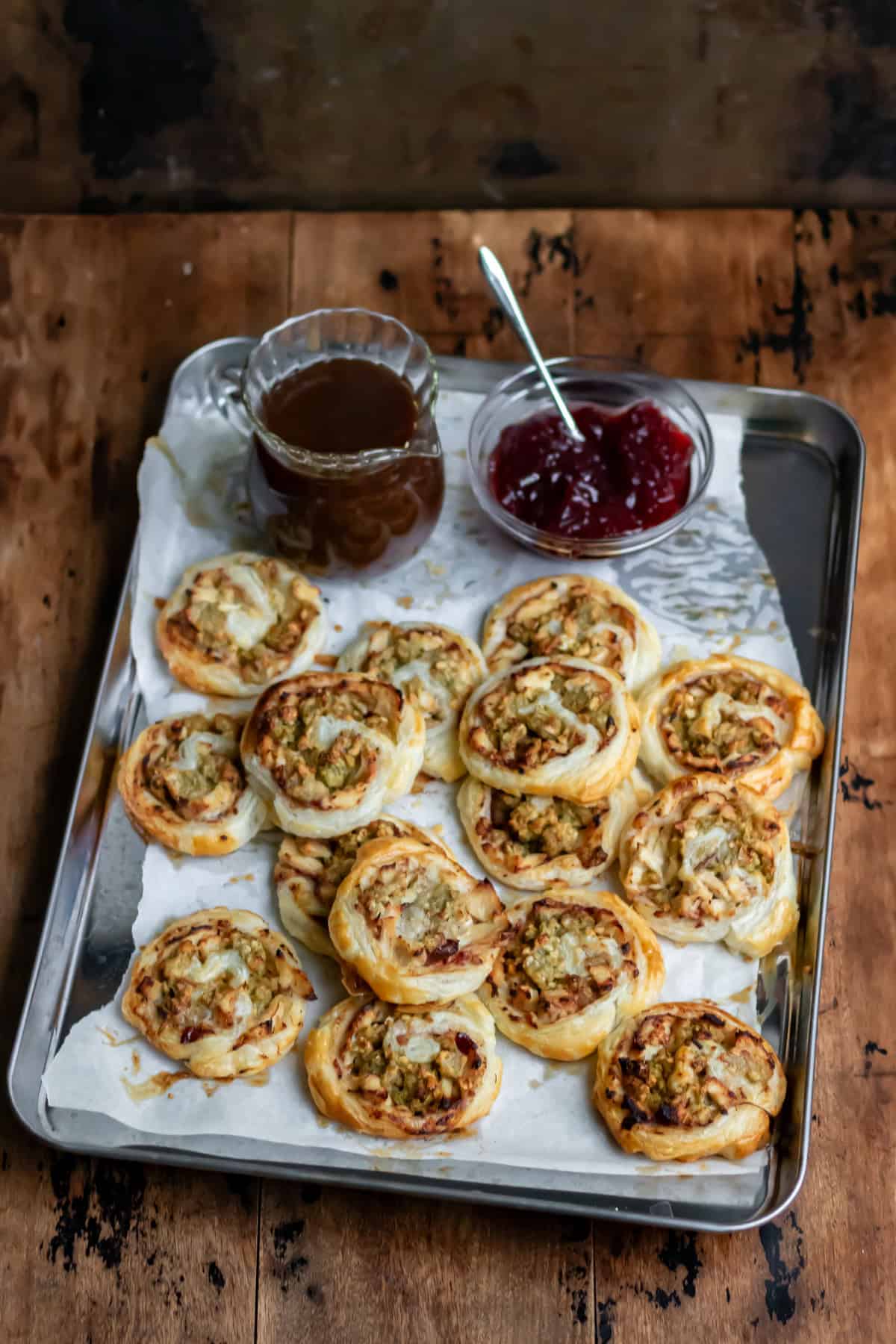 A table with a baking sheet of leftover turkey pinwheels, as well as a dish of cranberry sauce and a small glass jug of gravy.
