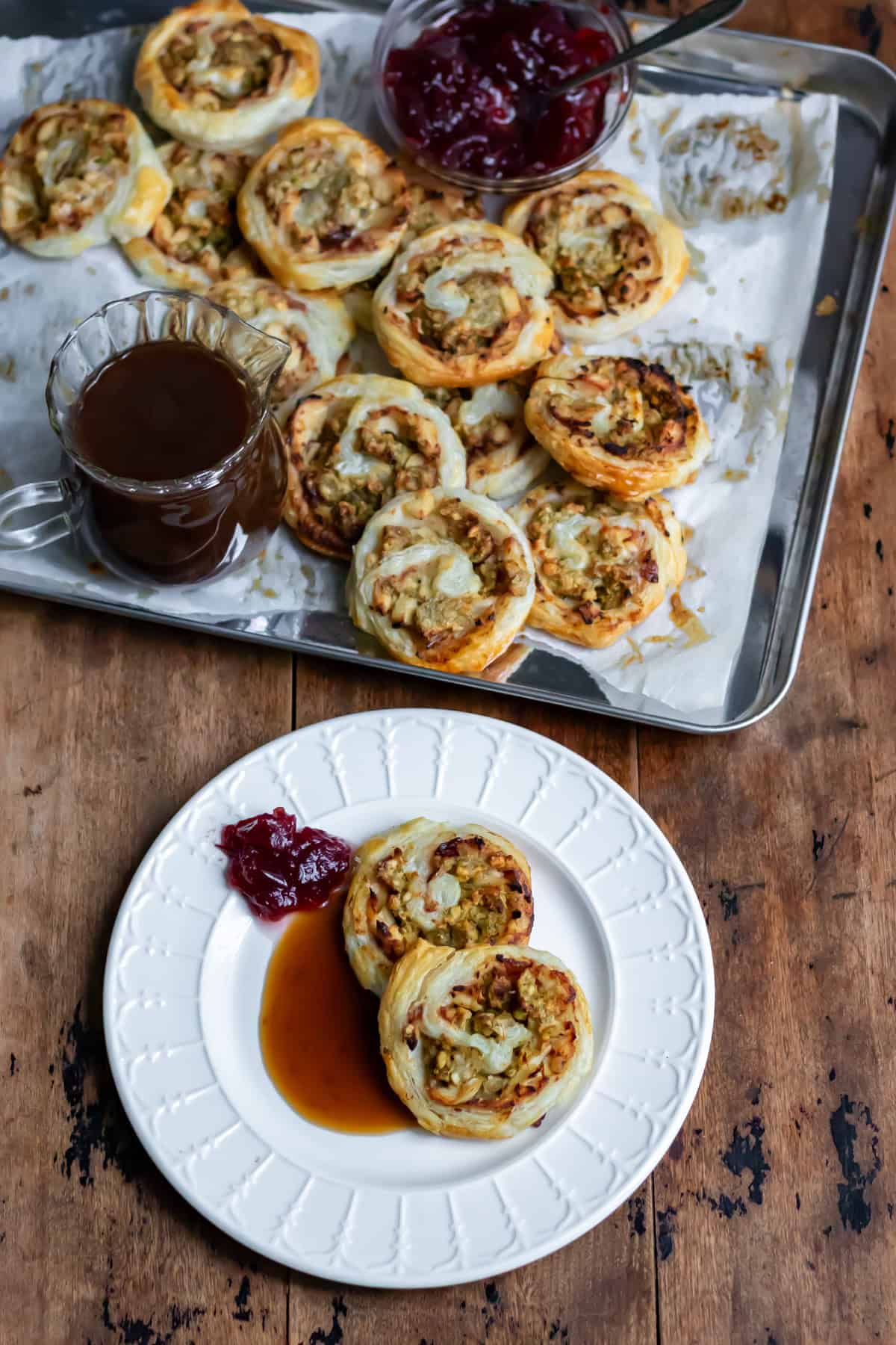 A table with a tray of leftover turkey pinwheels, as well as a plate with two of them plus gravy and cranberry sauce.