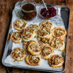 Leftover turkey pinwheels piled onto a baking sheet next to cranberry sauce and a jug of gravy.