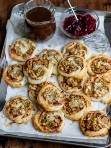 Leftover turkey pinwheels piled onto a baking sheet next to cranberry sauce and a jug of gravy.