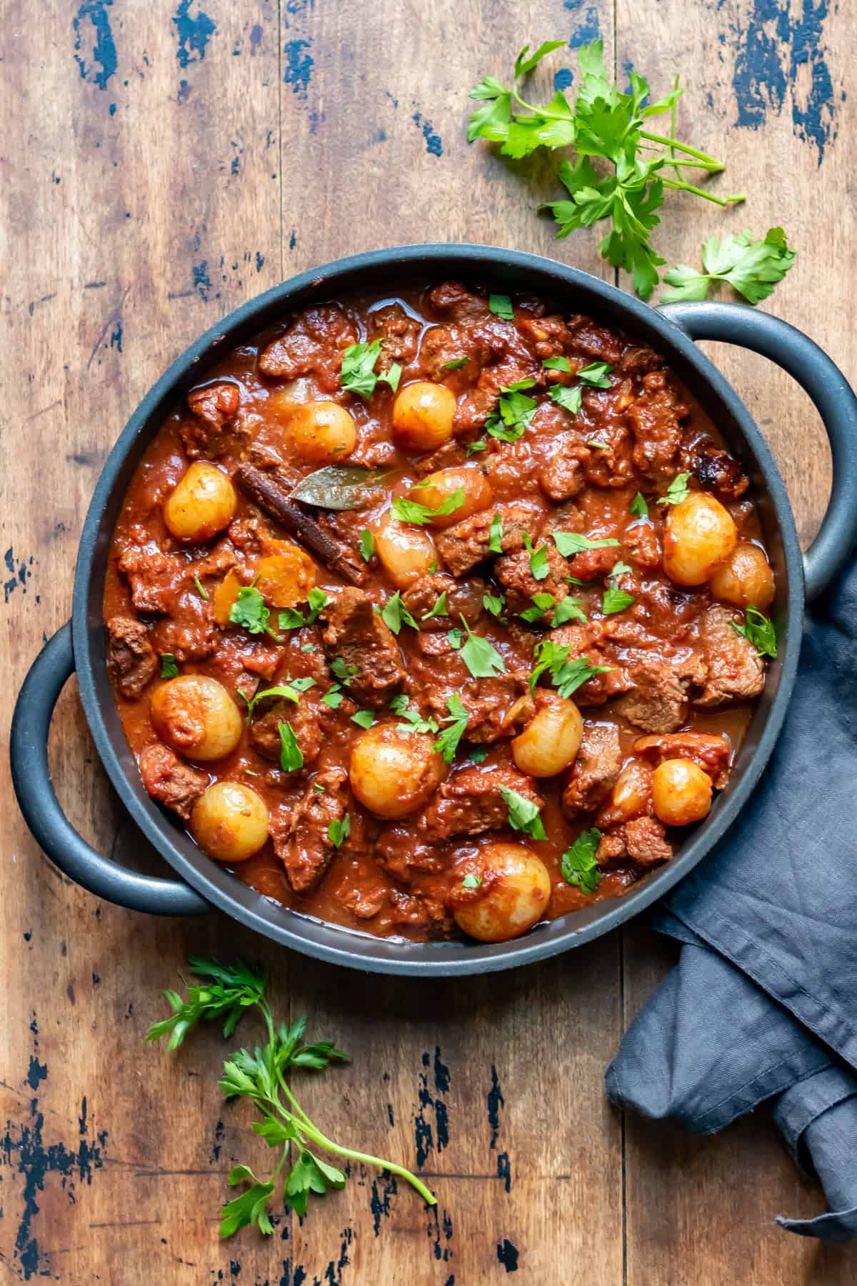 Wooden table with a serving dish of slow cooker stifado.