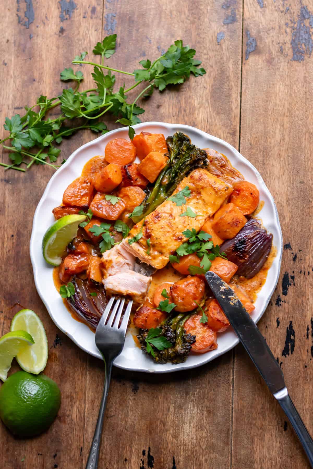 A wooden table with a plate of Thai salmon and veggies with a fork taking a bite out of the salmon.