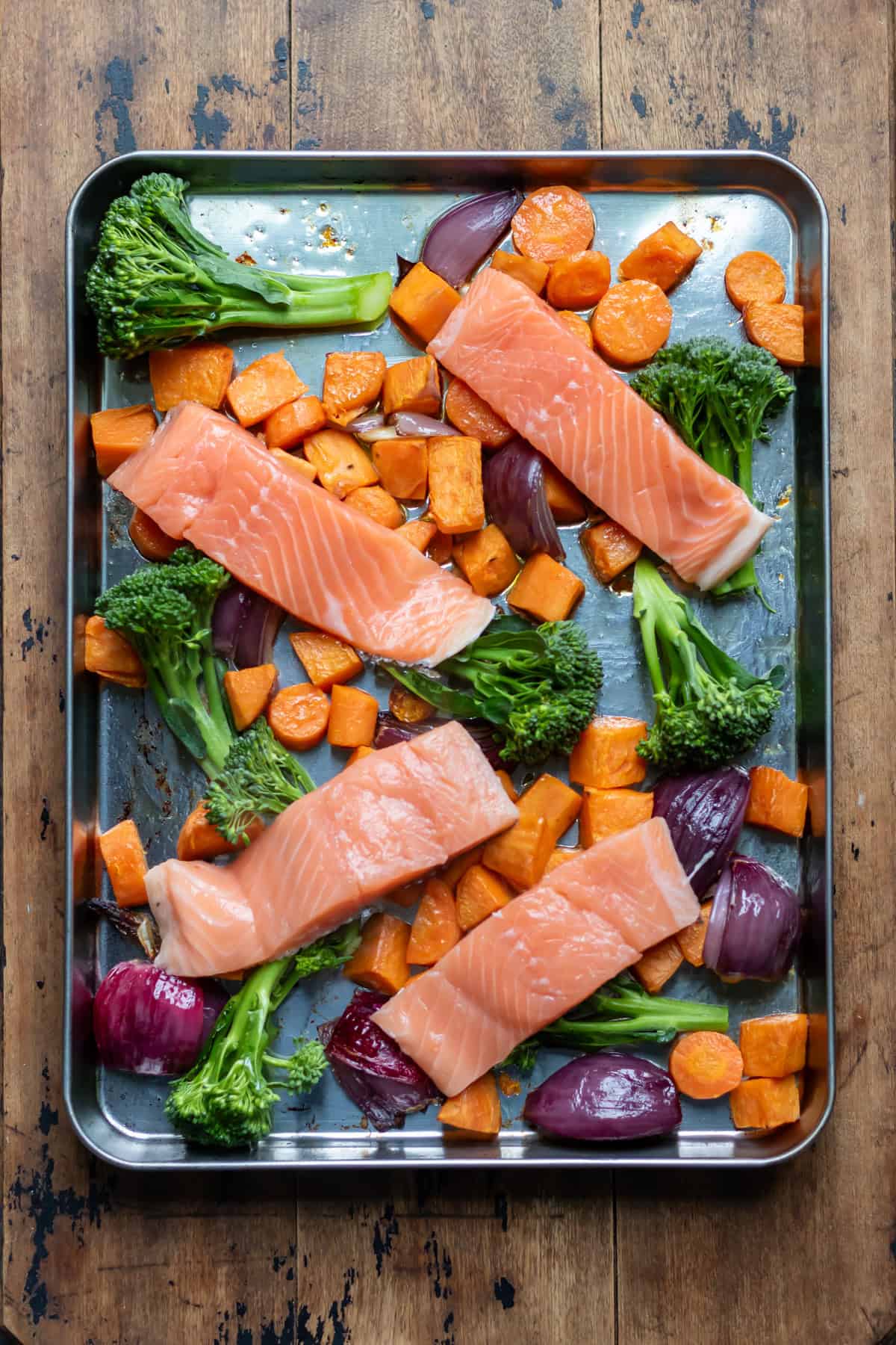 Fillets of salmon and broccoli added to the roasted vegetables on the baking sheet.