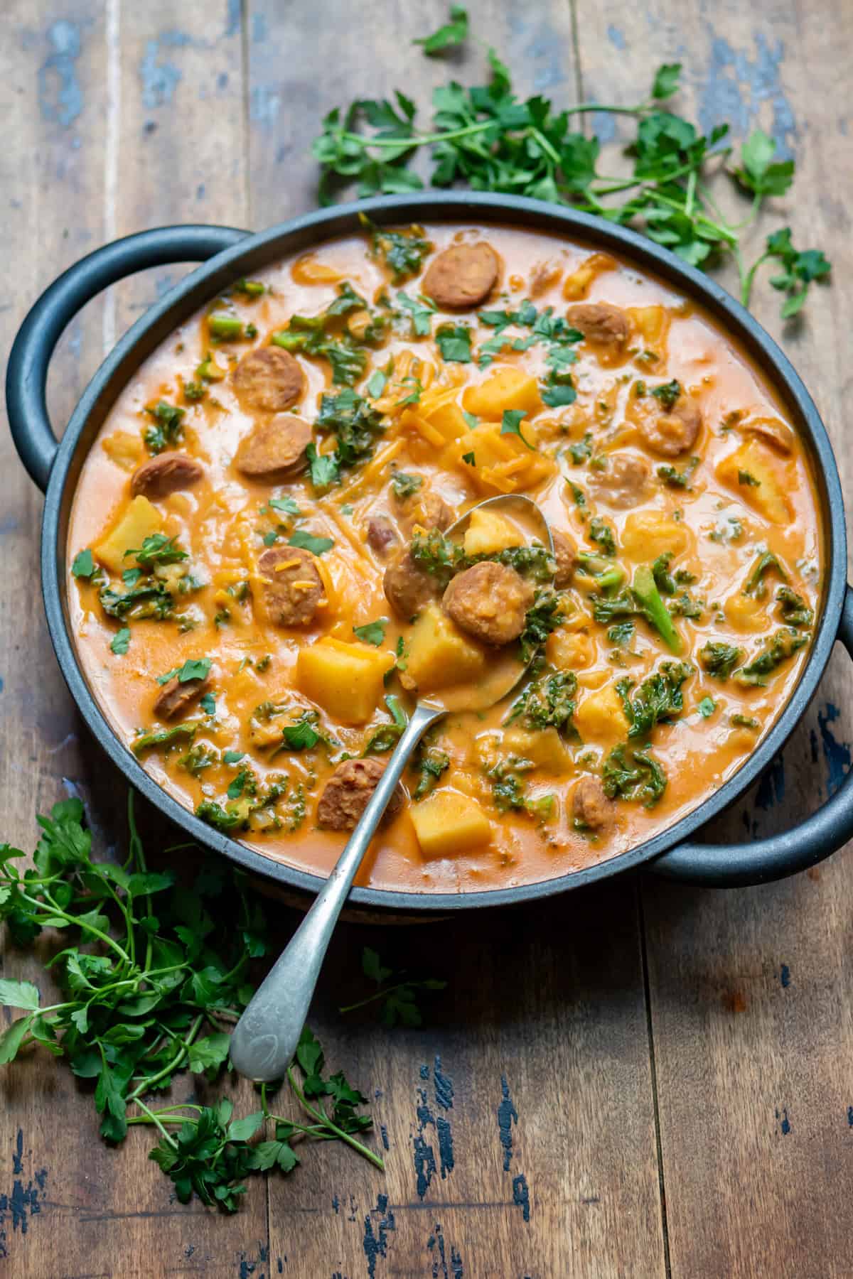 A serving spoon in a dish of creamy chorizo potato soup on a wooden table.