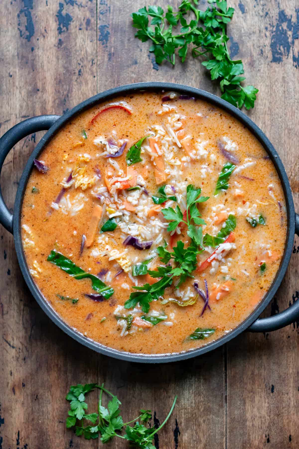 A wooden table with a serving dish of Thai Vegetable Soup with Rice.