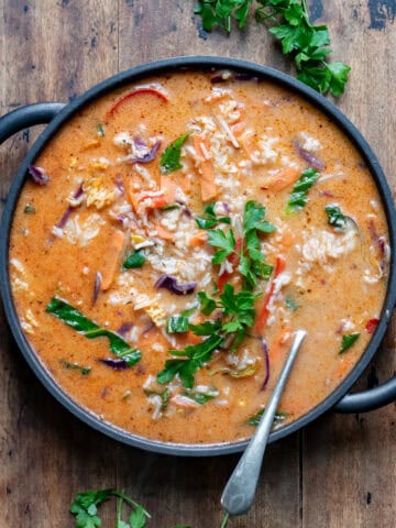 A wooden table with a serving dish of Thai Vegetable Soup with Rice.