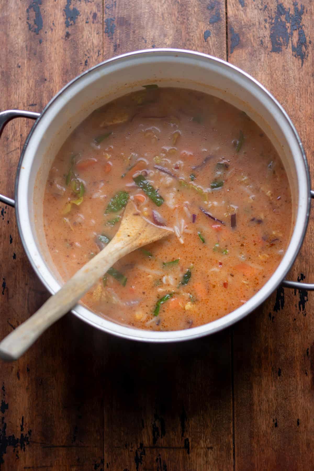 Finished thai vegetable soup with rice in a soup pot with a wooden spoon.