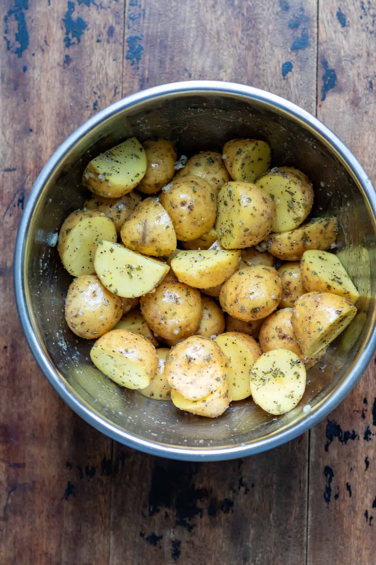 Baby potatoes coated in oil and seasonings in a bowl.