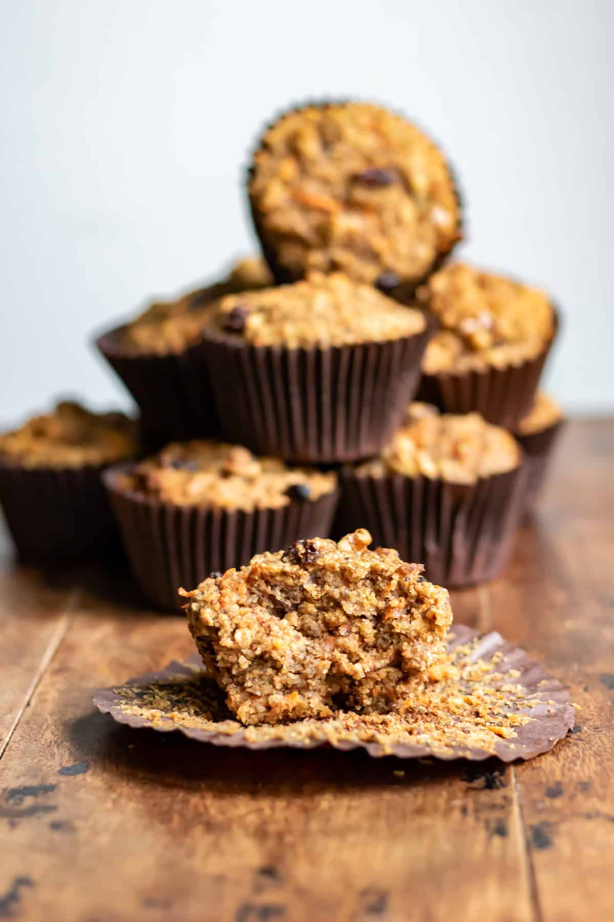 A carrot cake high fiber muffin with a bite out in front of a stack of muffins.