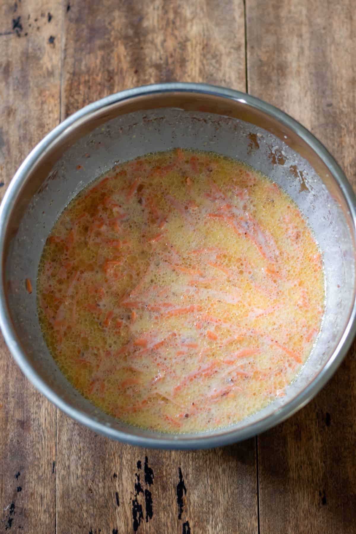 Wet ingredients mixed in a bowl, with shredded carrots.