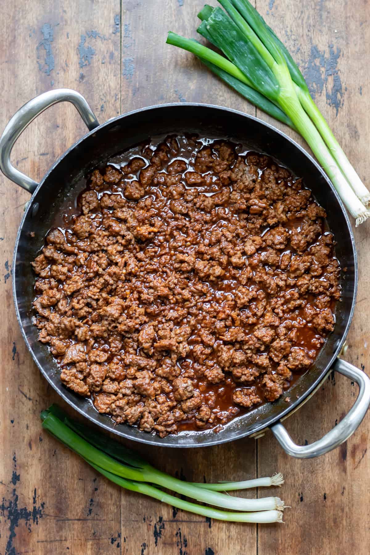 A pan of Korean ground beef on a wooden table next to spring onions.