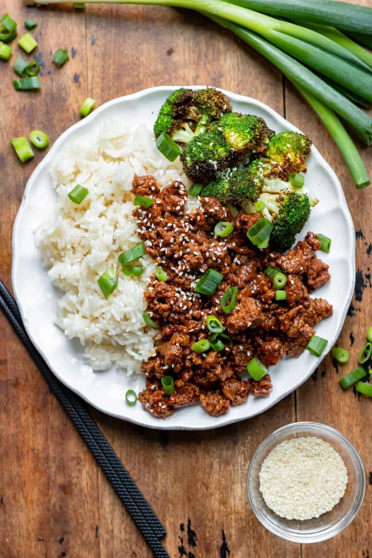 Looking down at a wooden table with a plate of rice, air fryer broccoli and Korean ground beef.