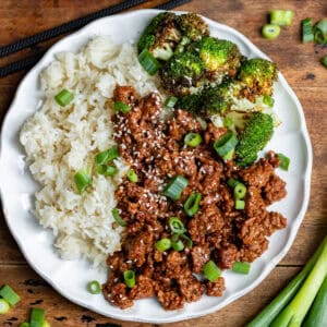 Looking down at a wooden table with a plate of rice, air fryer broccoli and Korean ground beef.