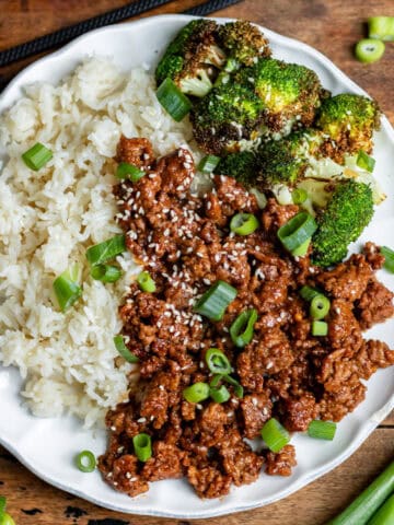 Looking down at a wooden table with a plate of rice, air fryer broccoli and Korean ground beef.