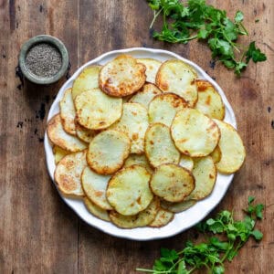 A plate of air fried potato slices, next to sprigs of parsley.
