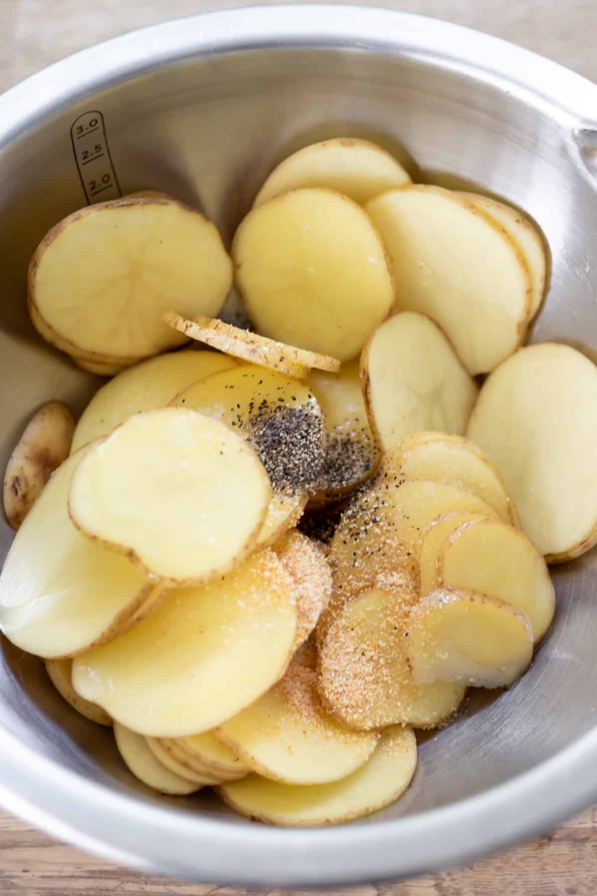 Sliced potatoes and seasonings in a bowl.