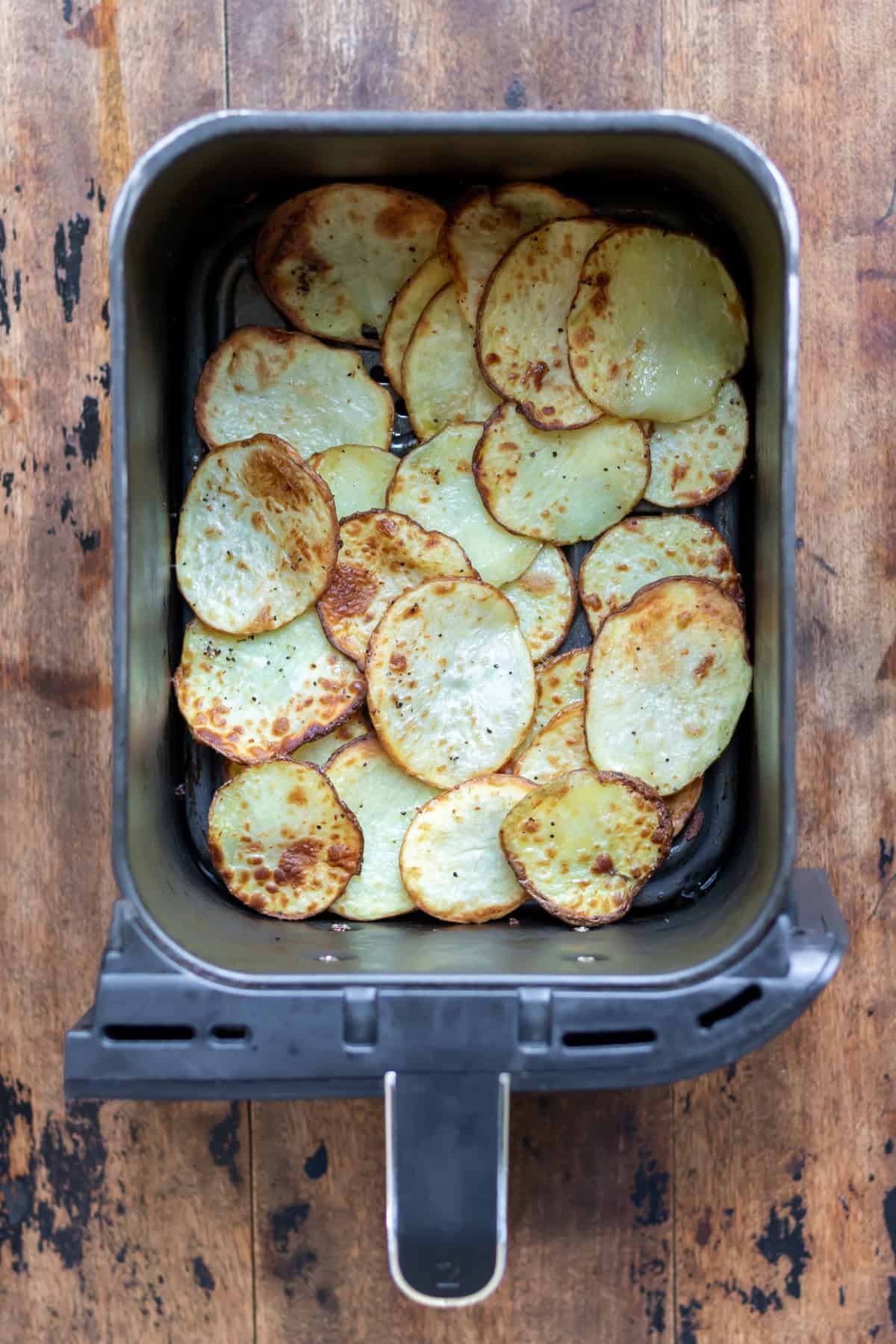 An air fryer basket filled with crispy sliced potatoes.