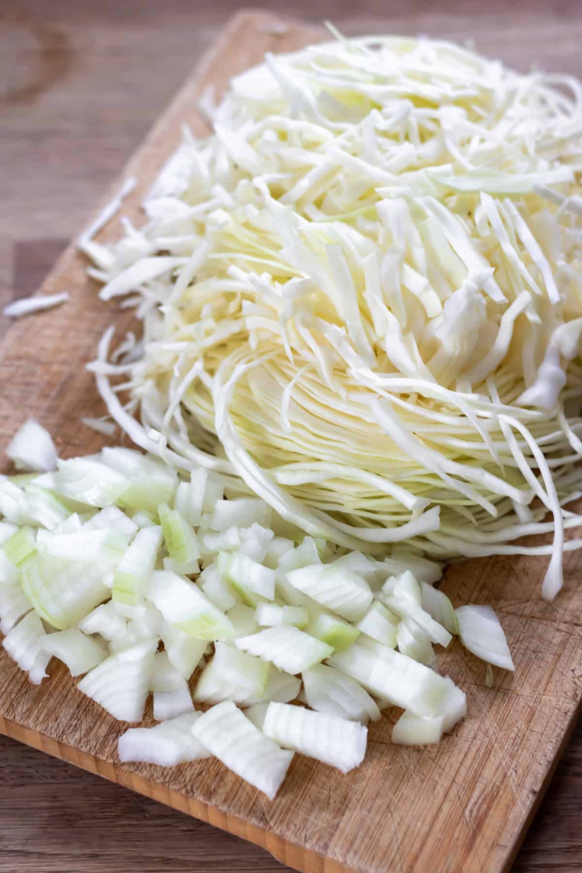 Sliced cabbage and diced onion on a chopping board.
