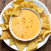 A table with a bowl of nacho cheese sauce, with one tortilla chip in the dip, and surrounded by more chips.