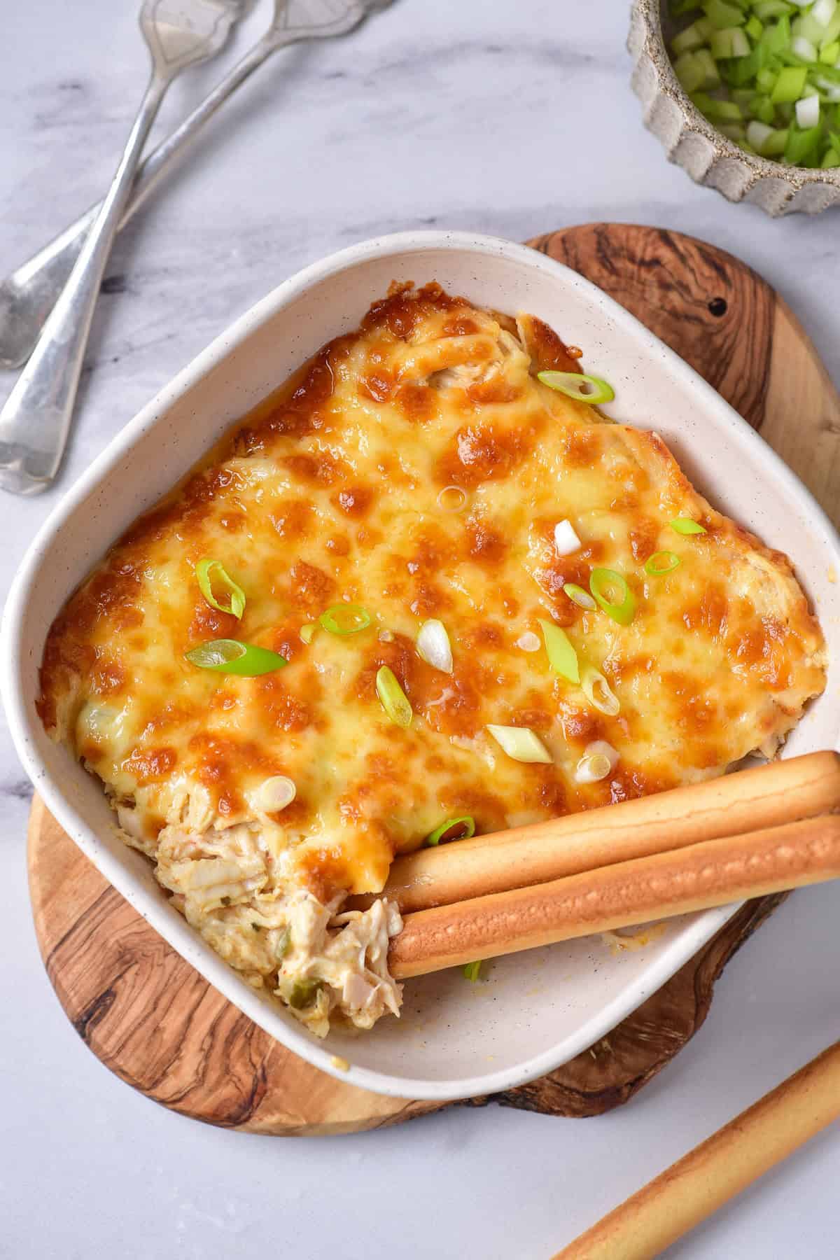 Looking down at a table with a serving dish of baked Buffalo ranch chicken dip.