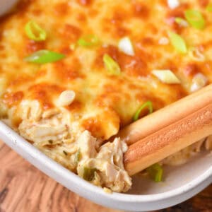 Close up of breadsticks in a dish of baked Buffalo ranch chicken dip.
