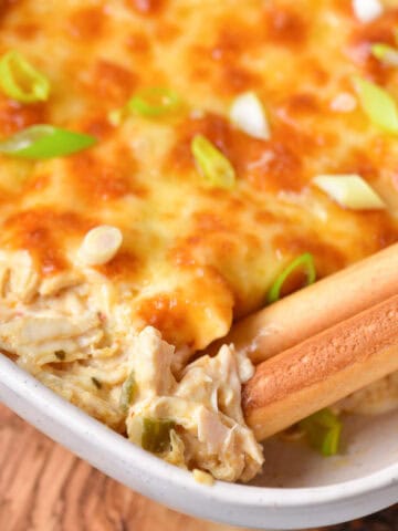 Close up of breadsticks in a dish of baked Buffalo ranch chicken dip.
