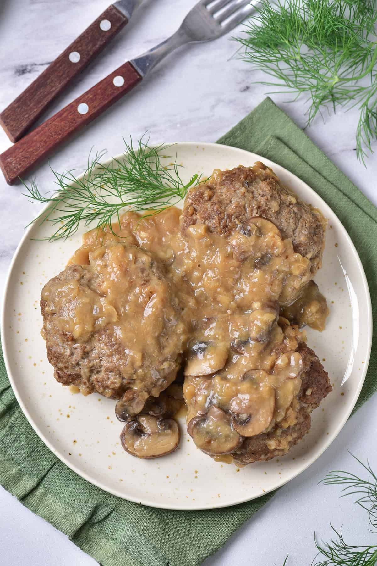 Looking down at a serving dish of salisbury steaks with mushroom gravy,