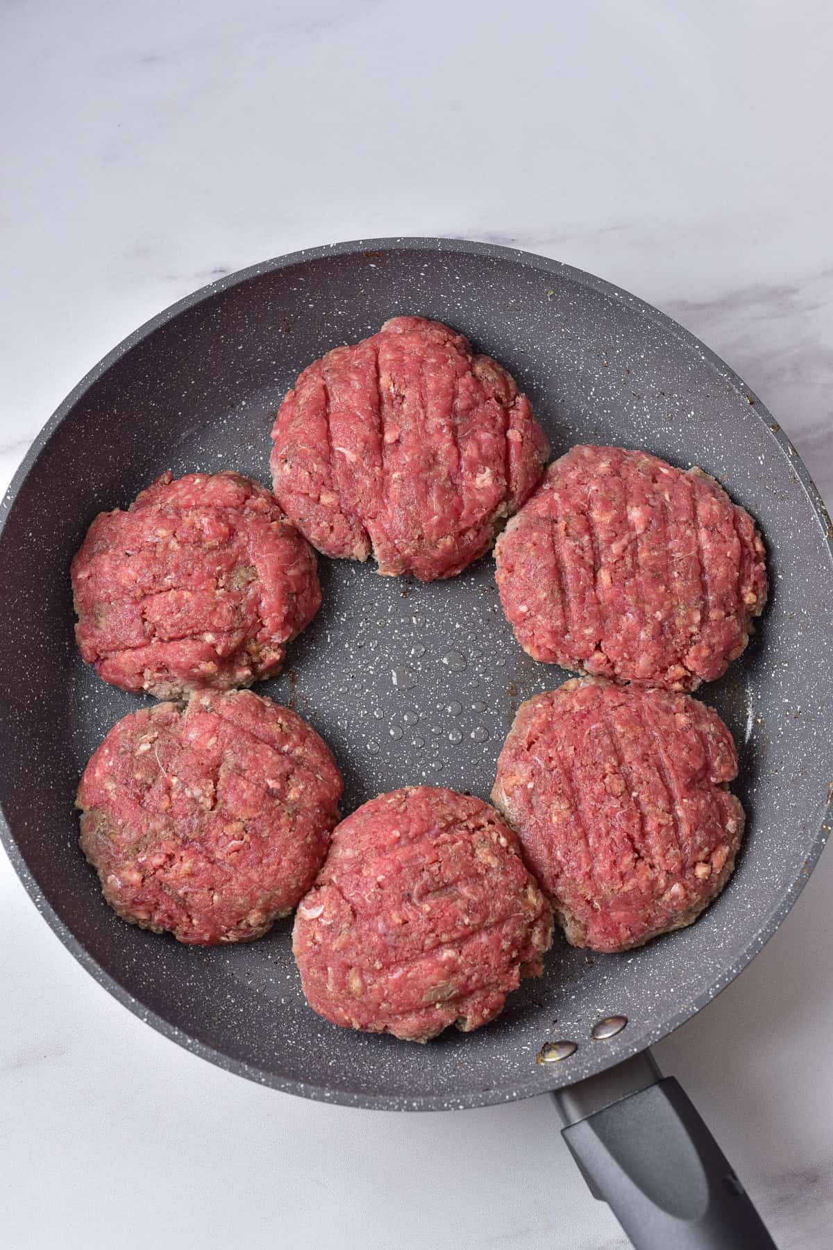Meat patties added to a skillet.