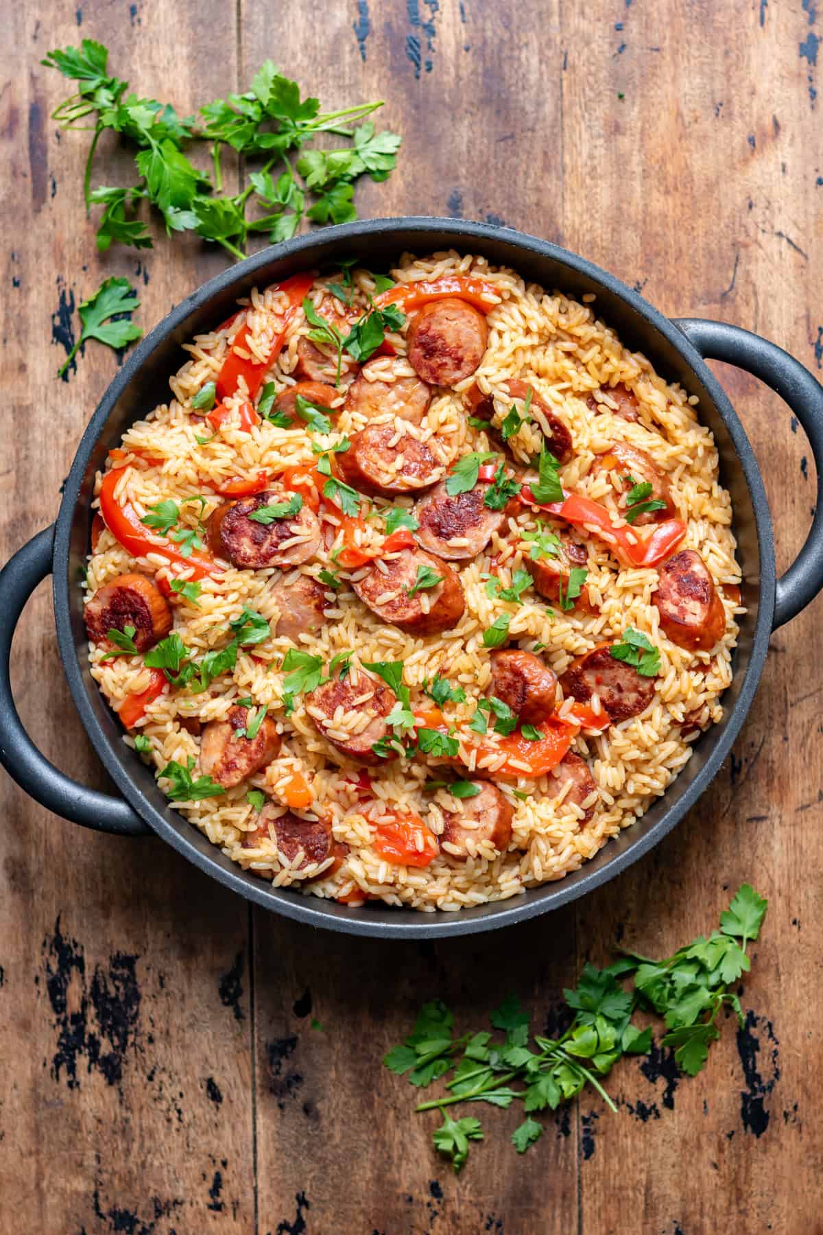 Wooden table with a serving dish of one pan smoky sausage rice skillet.