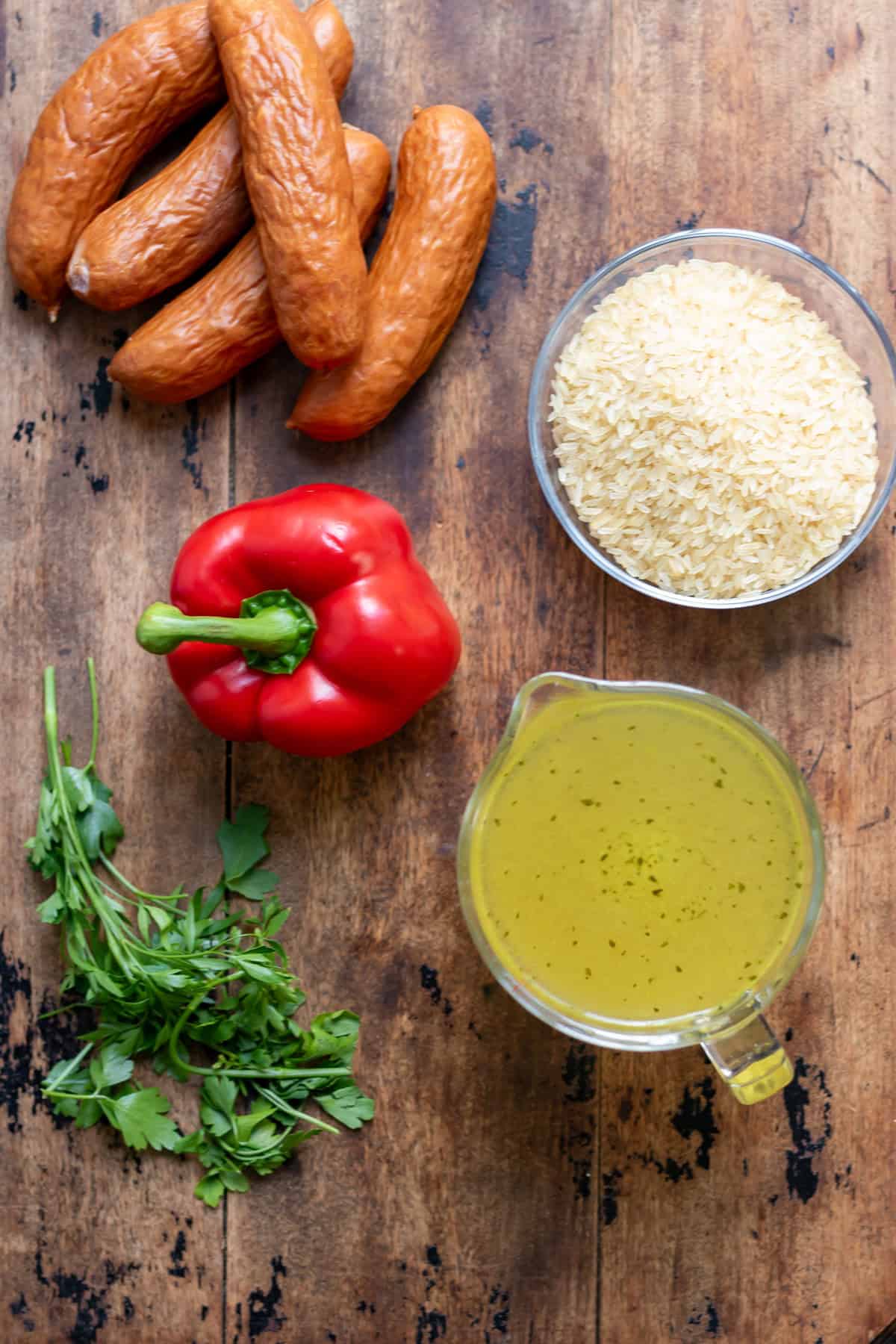 Kielbasa, rice, stock, red bell pepper and parsley on a table.