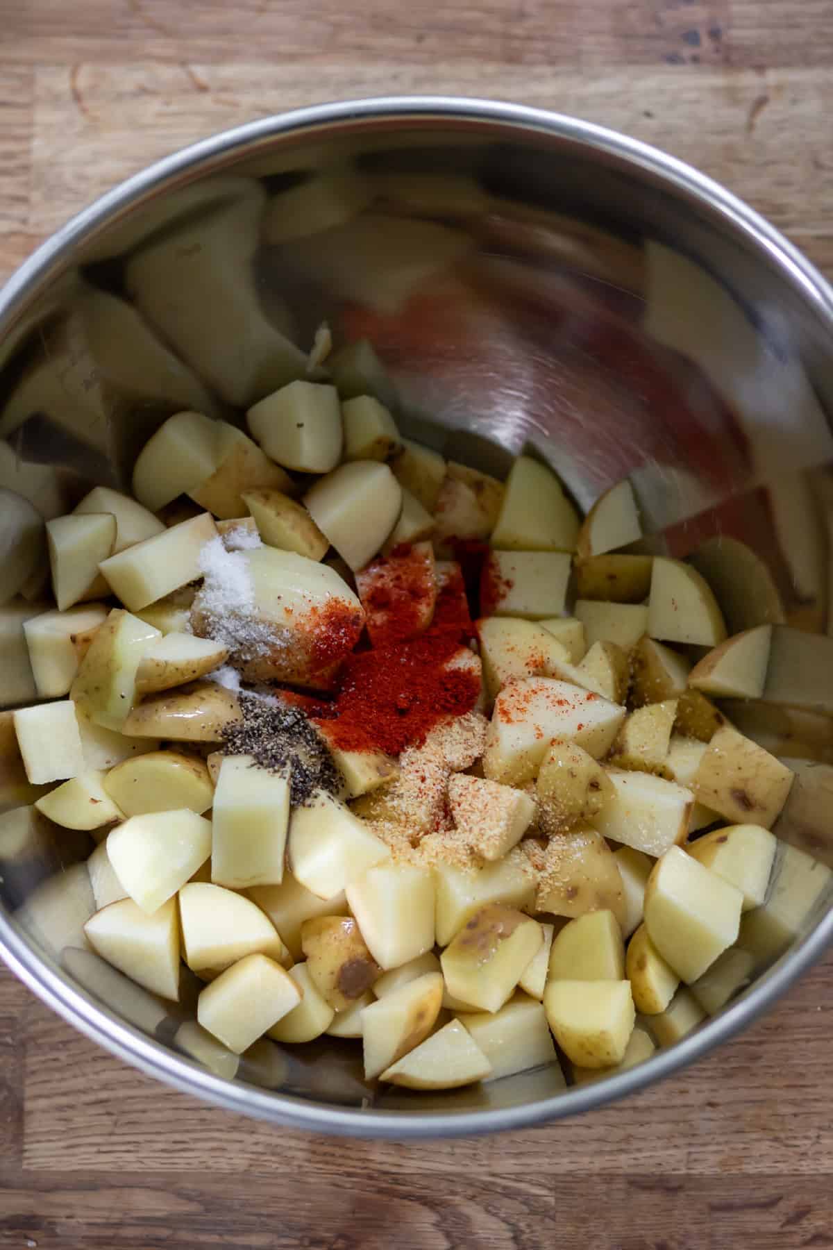 Diced potatoes in a bowl with the seasonings and oil.