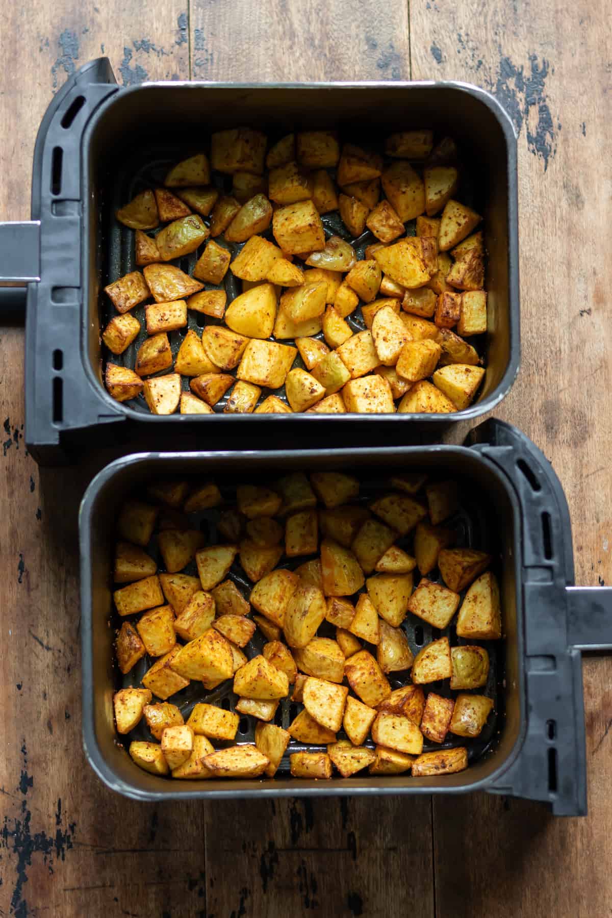 Cooked crispy air fryer diced potatoes in the air fryer baskets.
